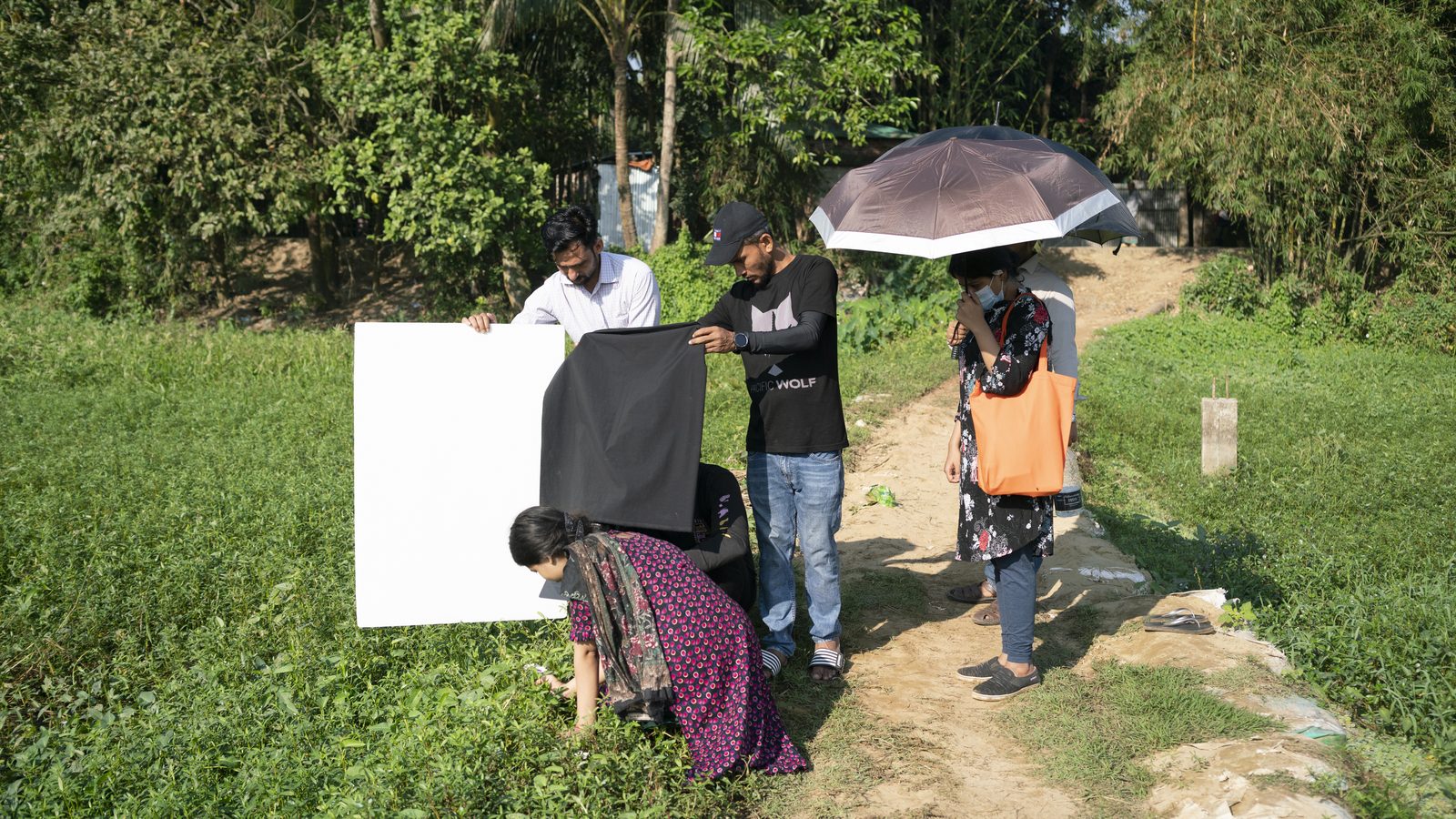Crew with a reflector and camera filming a girl walking through a green field in Bangladesh
