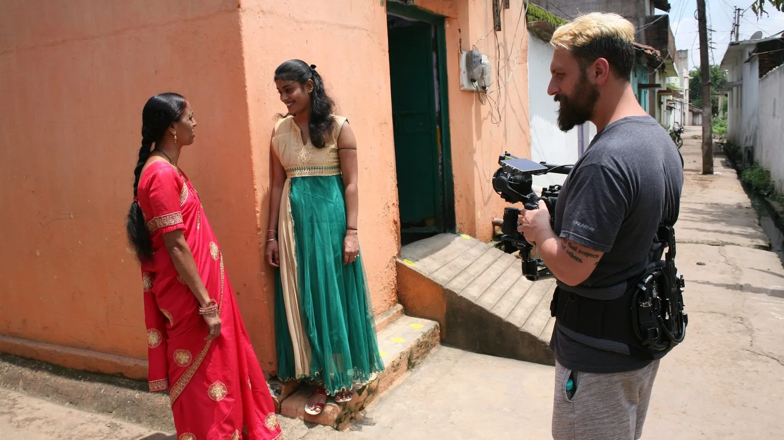 Camera operator filming two women on a painted porch in India