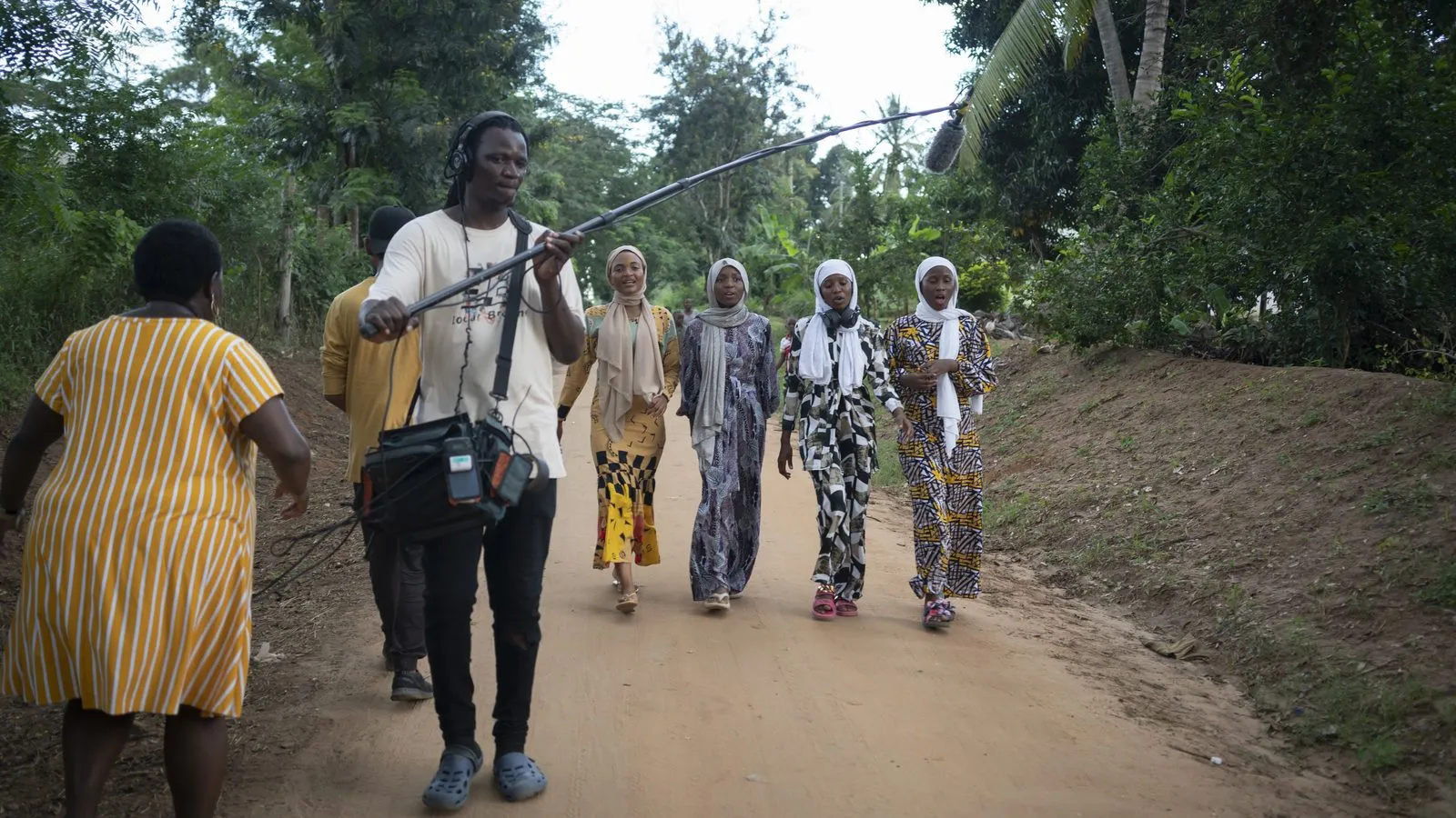 Crew walking a dirt road alongside a line of women in Tanzania
