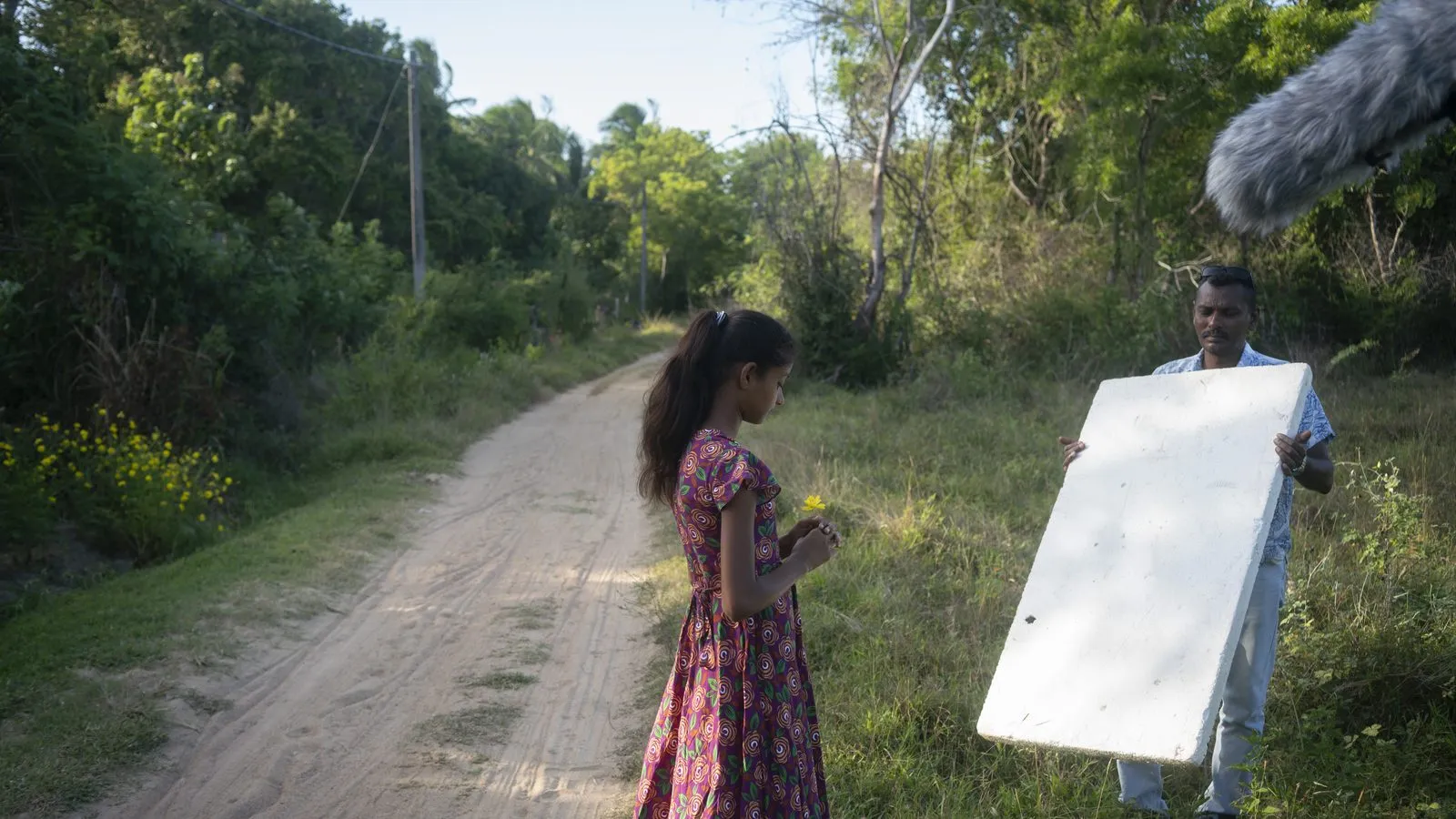 Crew member holding a reflector for a girl on a dirt road in Sri Lanka