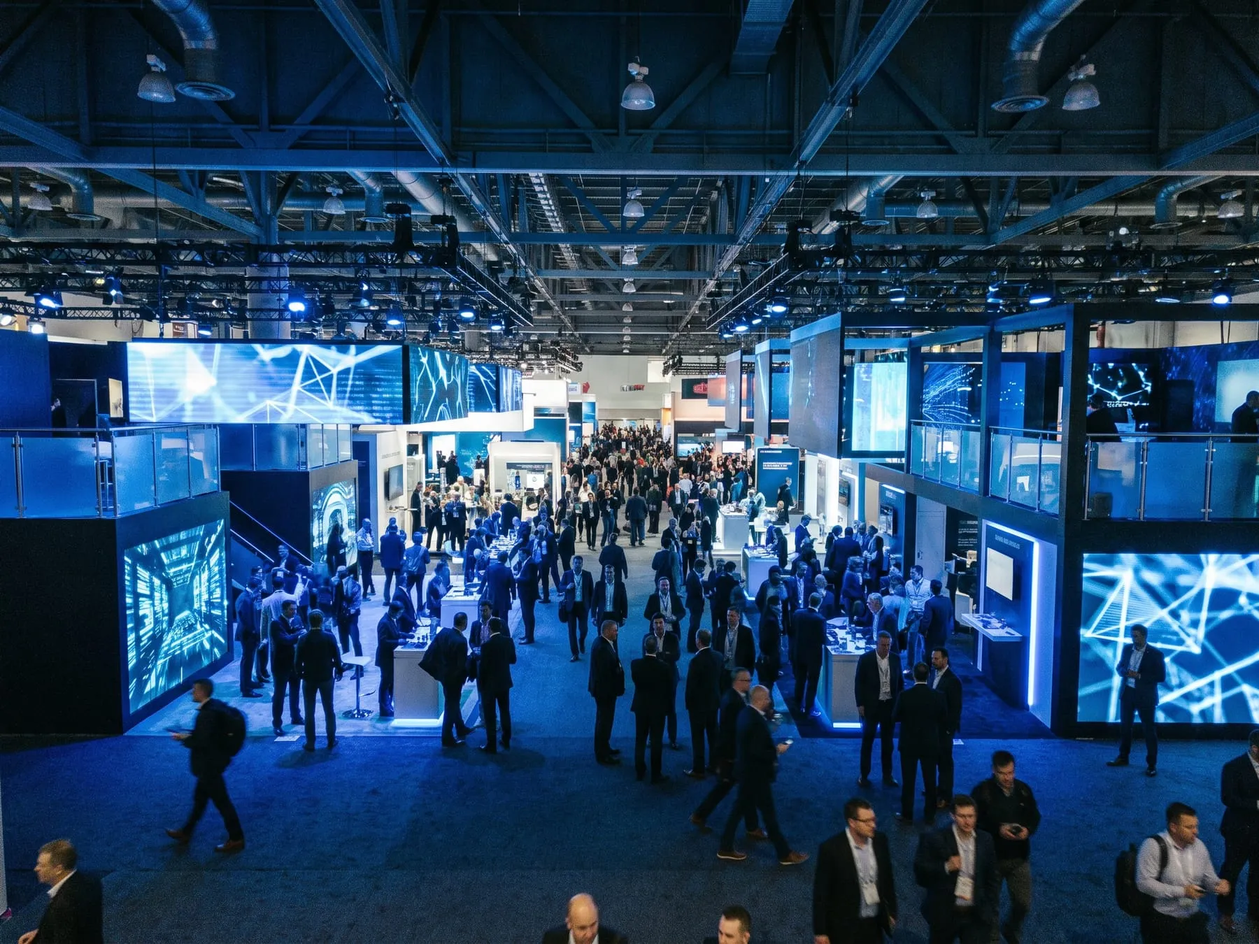 Expo hall with tall booths and glowing LED walls, attendees in the aisles