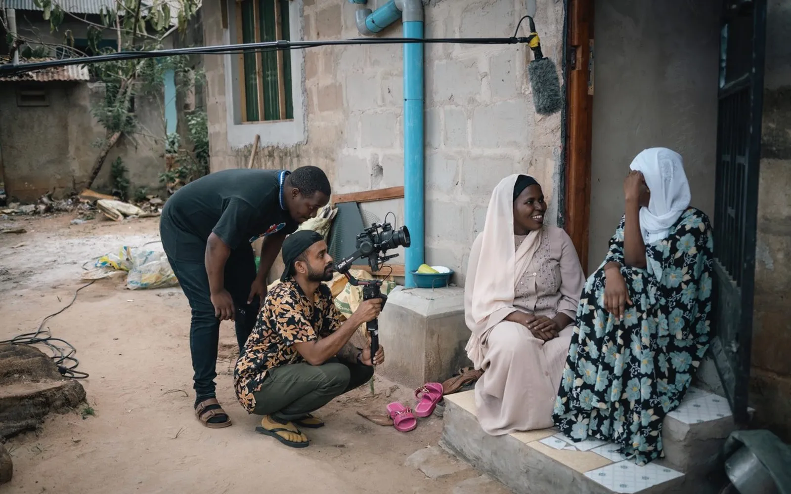 Camera operator filming two women seated outside a house in Sri Lanka