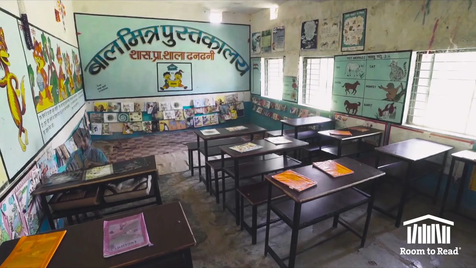A painted children's library in a Nepali school, low desks with open books and a mural over the door, a frame from the Room to Read film