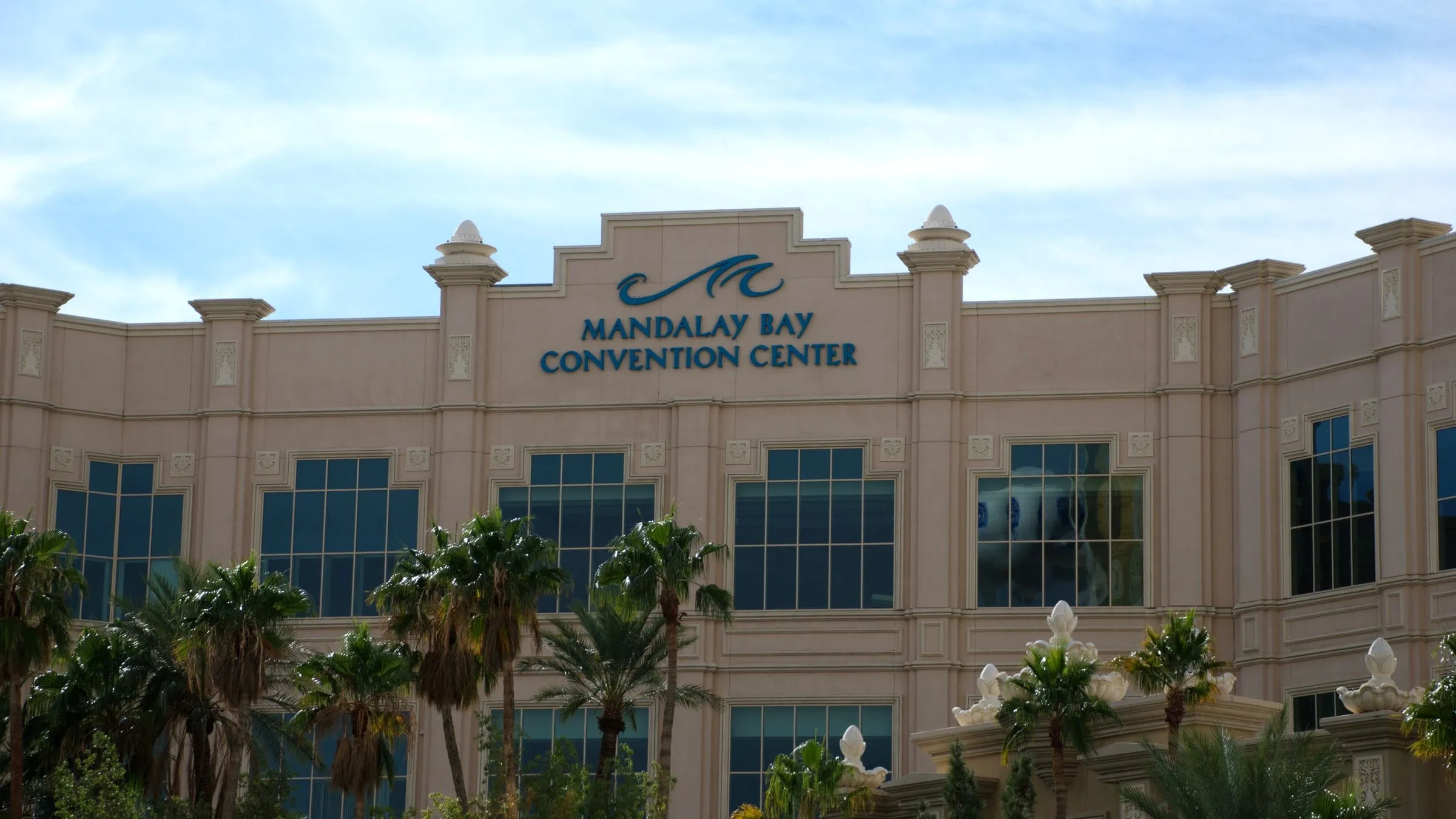 The front of the Mandalay Bay Convention Center in Las Vegas, its name on the facade above a row of palms