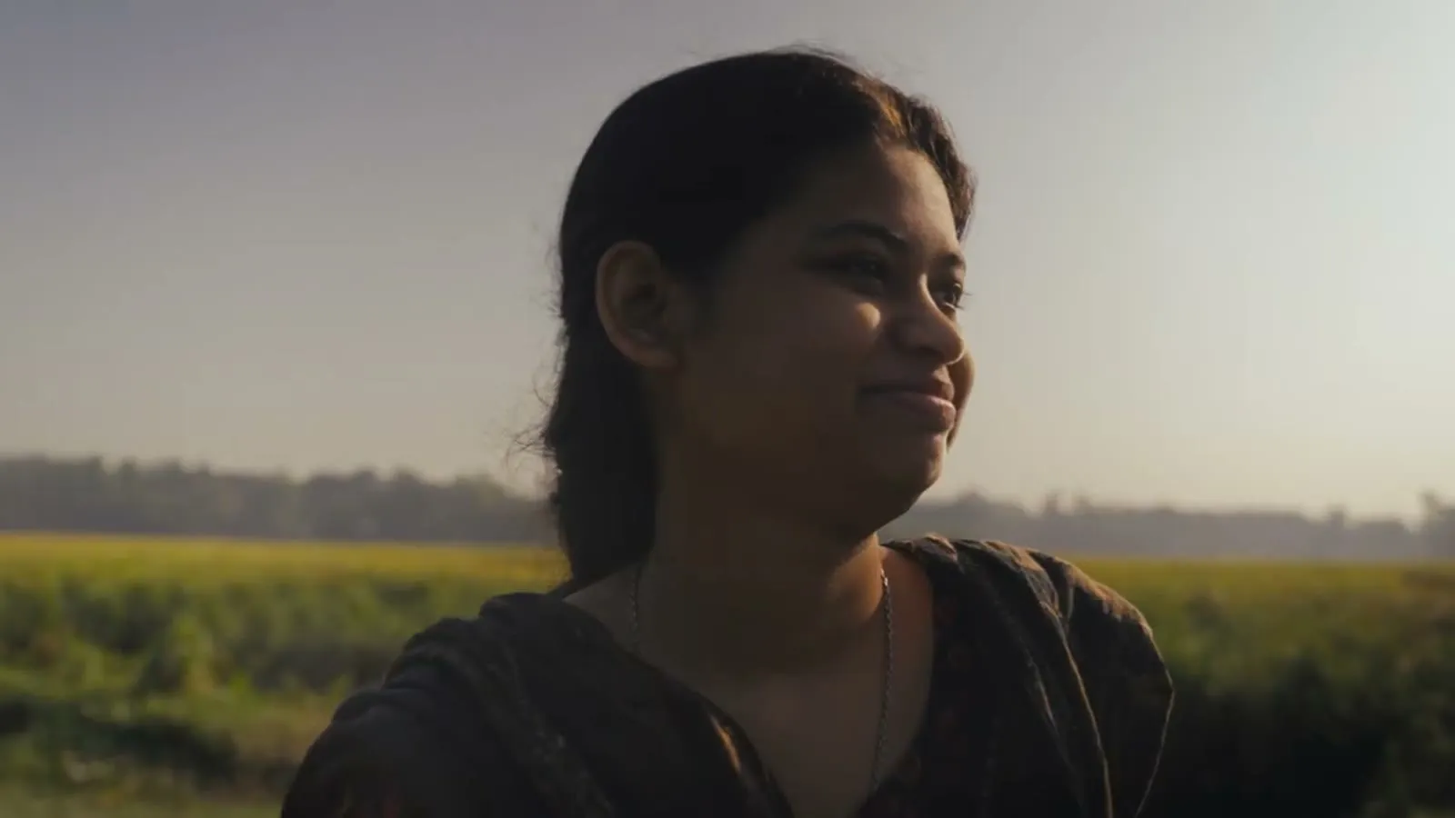 A young woman smiles in golden hour light in a rural field, from a Room to Read documentary