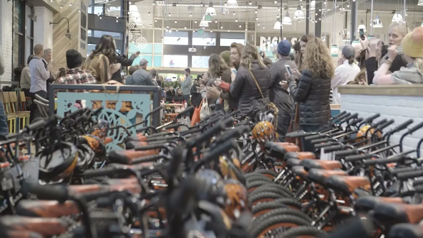 Rows of new orange kids' bikes lined up inside a Whole Foods Market under string lights, from the store opening promo