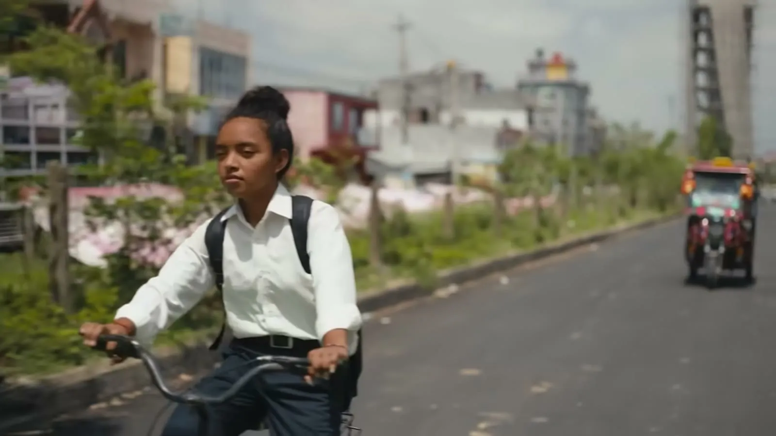 A girl rides a bicycle down a road, a still from the She Creates Change documentary trailer