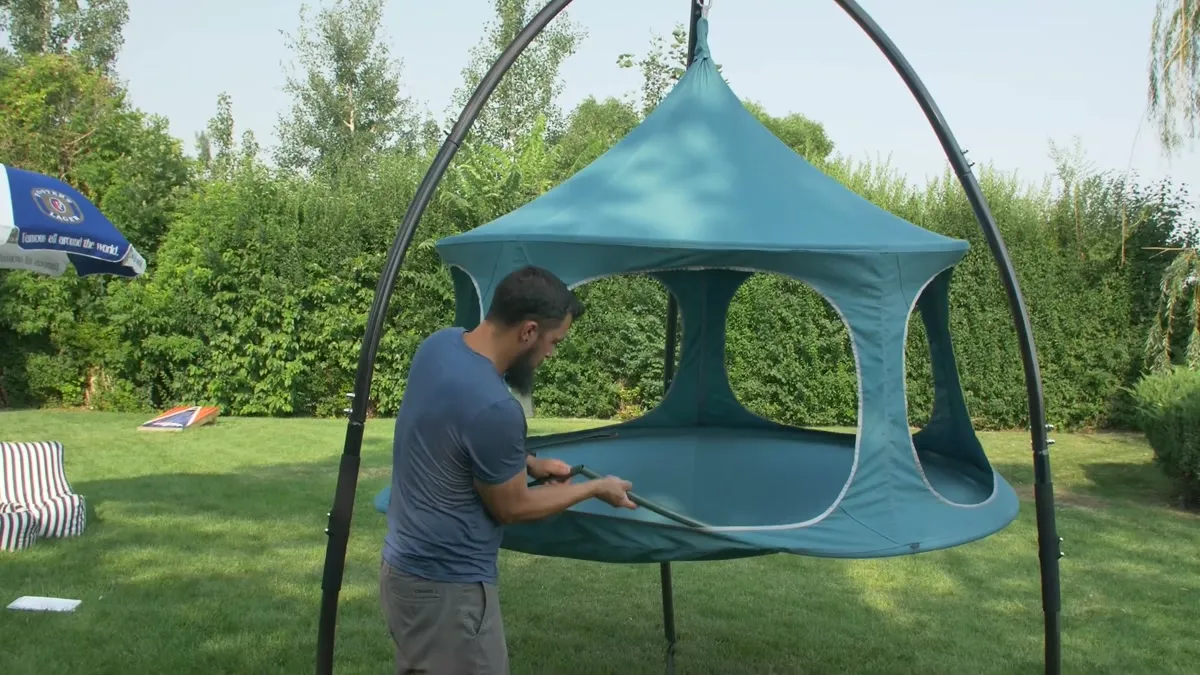 A man assembling a teal Canopy TreePod hanging pod in a backyard
